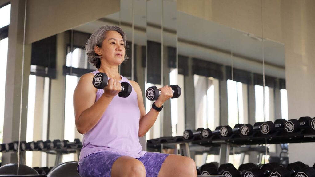 Photo of asian woman in a gym. she is seated while curling dumbells.