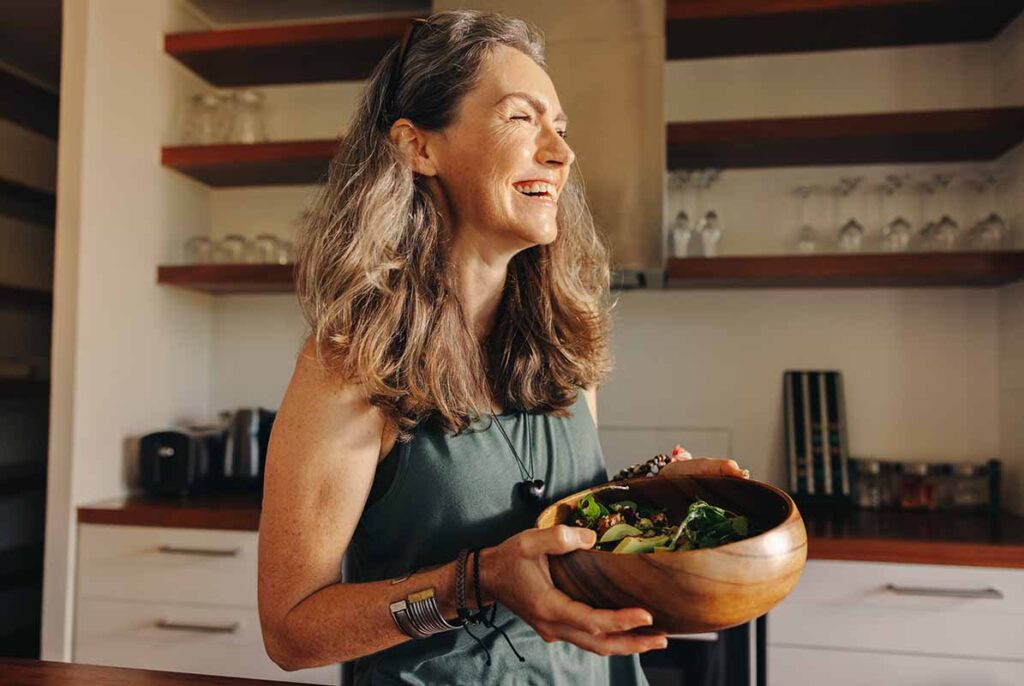 photo of health-looking middle aged white with loose long carrying a wooden salad bowl and smiling.